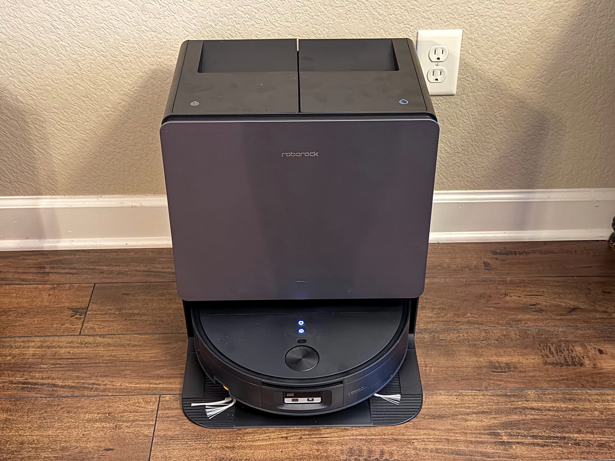 Black Roborock Saros 20 Flow robot vacuum sitting inside its matching docking station against a beige wall.