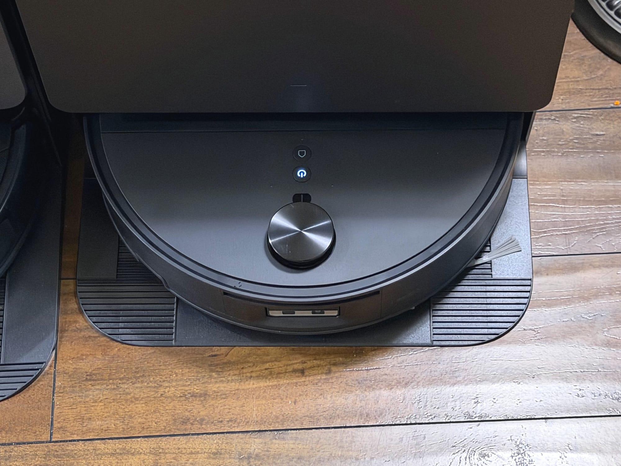 Close-up of the black Roborock Saros 20 Flow robot vacuum resting on its docking ramp, showing the blue illuminated power button and raised lidar sensor.