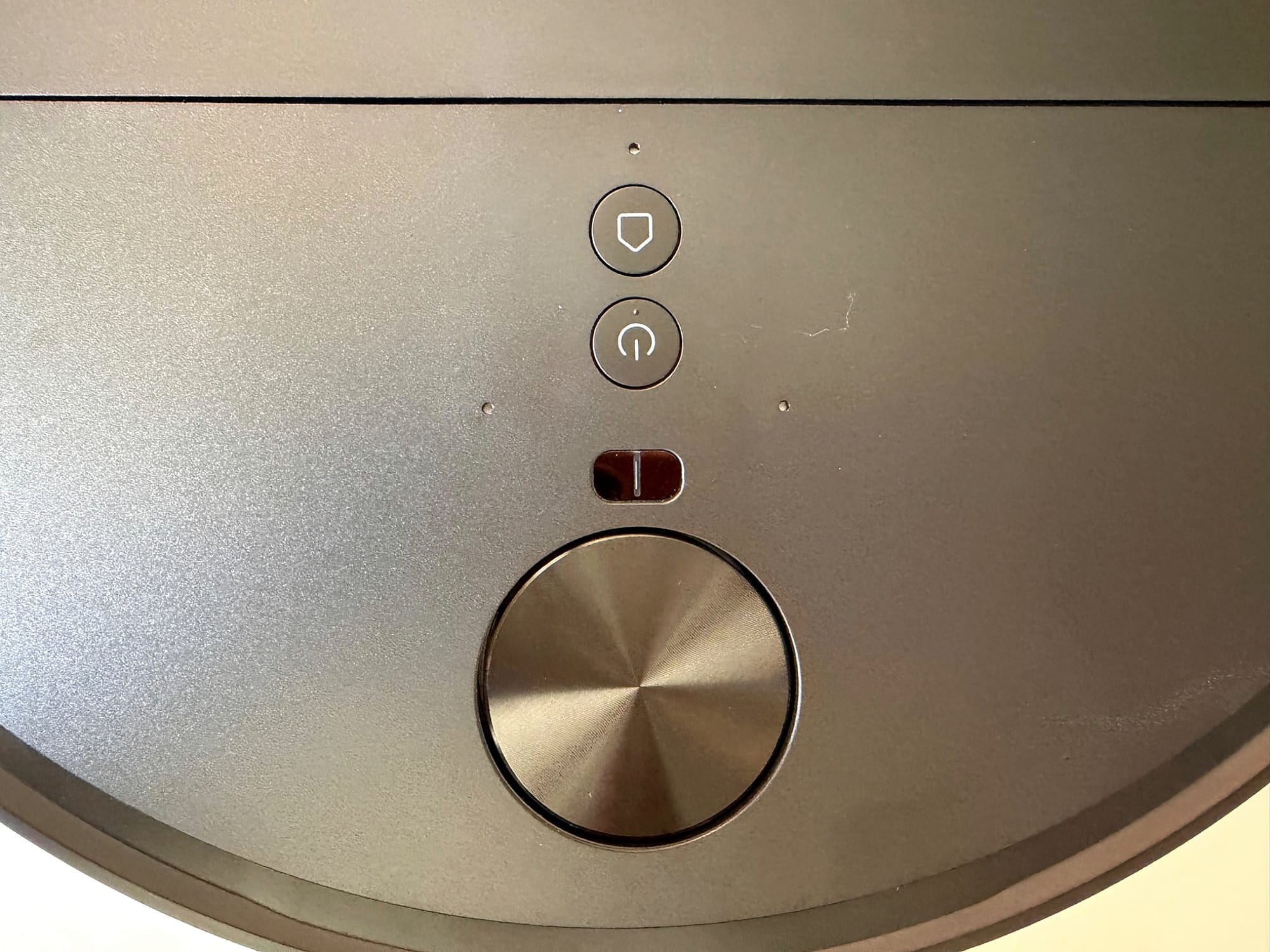 Overhead view of the black Roborock Saros 20 Flow robot vacuum on brown hardwood flooring, showing its circular lidar sensor, illuminated controls and front obstacle avoidance sensors.