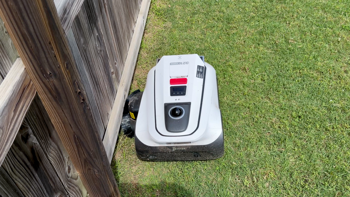 Ecovacs GOAT A2000 LiDAR Pro robotic mower cutting grass beside a wooden backyard fence.