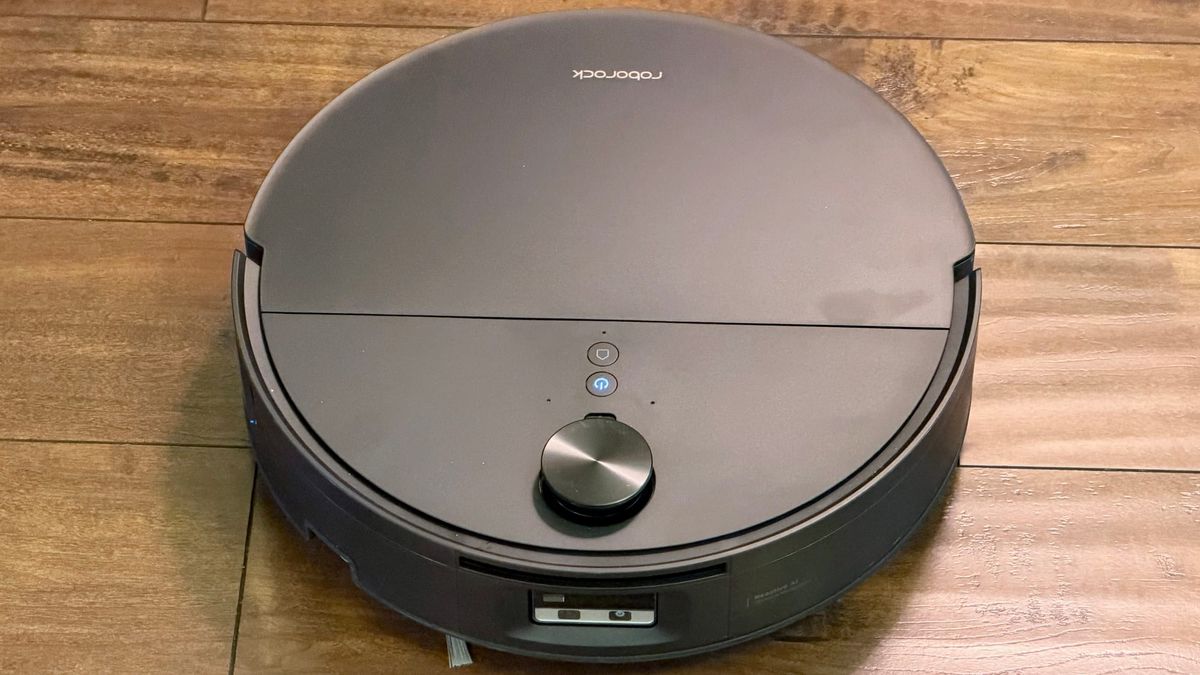 Black Roborock Saros 20 Flow robot vacuum on hardwood flooring, showing its retractable lidar sensor, illuminated power button and front obstacle avoidance sensors.