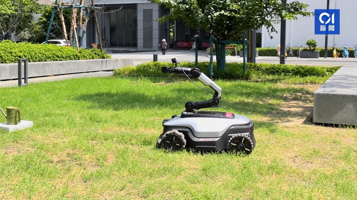 Dreame NexLawn robot mower on a lawn with its articulated arm extended and a green watering can nearby.