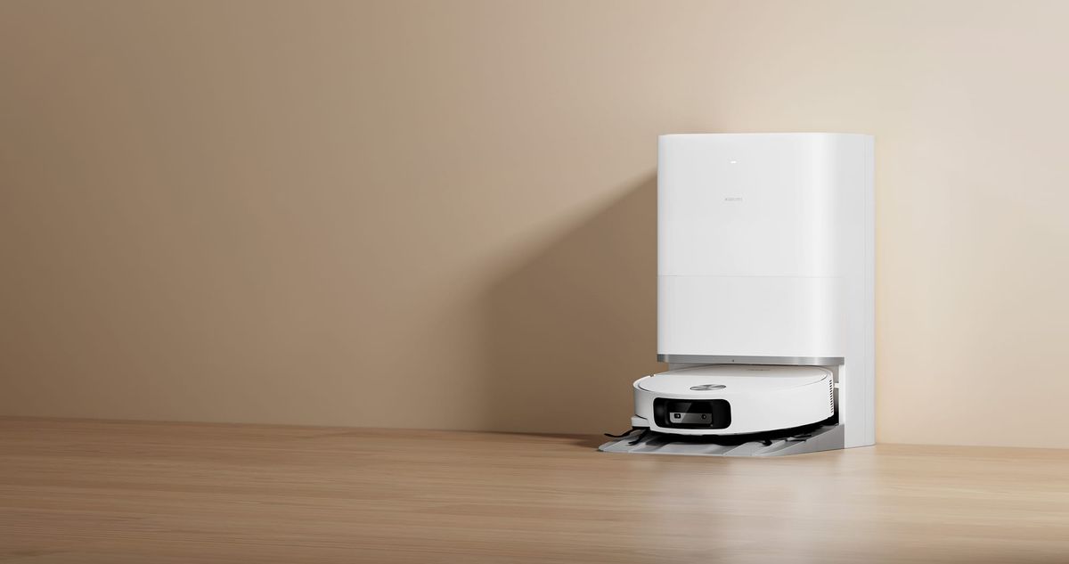 White Xiaomi Robot Vacuum 6 docked at its matching cleaning station on a wood floor against a beige wall.