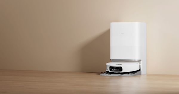 White Xiaomi Robot Vacuum 6 docked at its matching cleaning station on a wood floor against a beige wall.