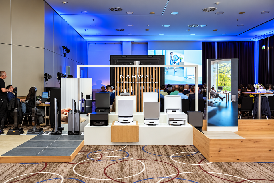 Narwal’s IFA 2026 booth with robot vacuums and docking stations on a central display, cordless cleaners on the left and attendees seated behind the exhibit.