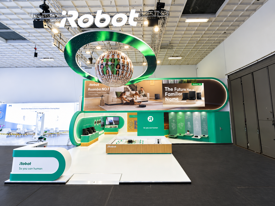 Wide view of the iRobot booth at IFA 2026, with a large illuminated logo, suspended circular display and green-and-white product exhibits.
