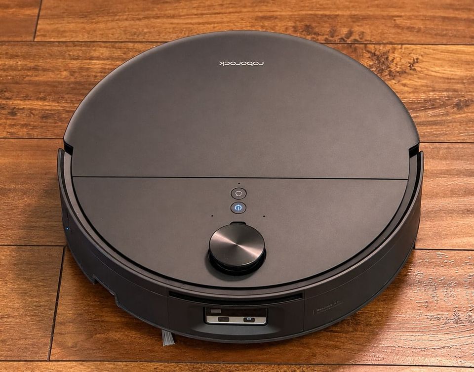 Black Roborock Saros 20 Flow robot vacuum on hardwood flooring, showing its retractable lidar sensor, illuminated power button and front obstacle avoidance sensors.