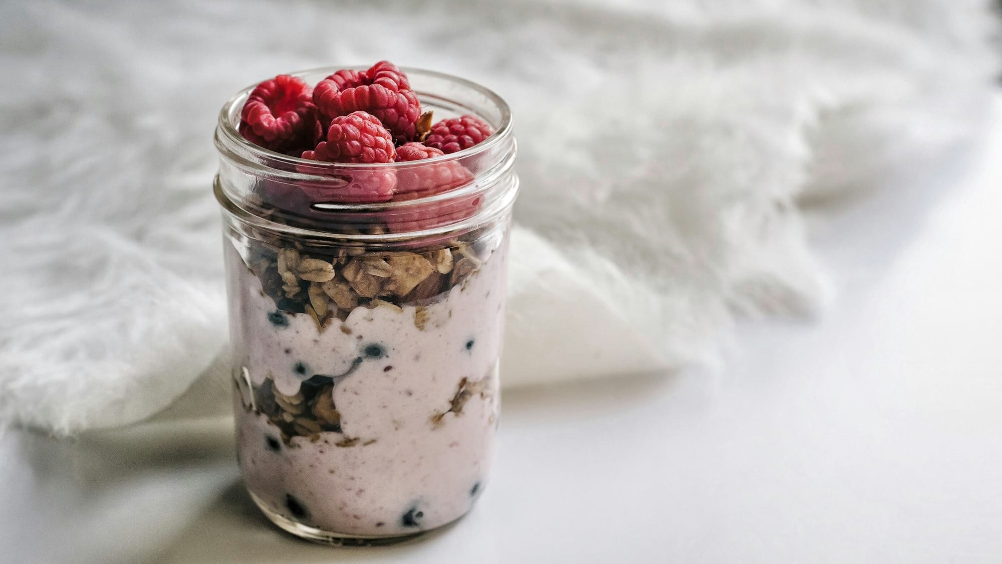 Granola, raspberries and yoghurt filled mason jar.