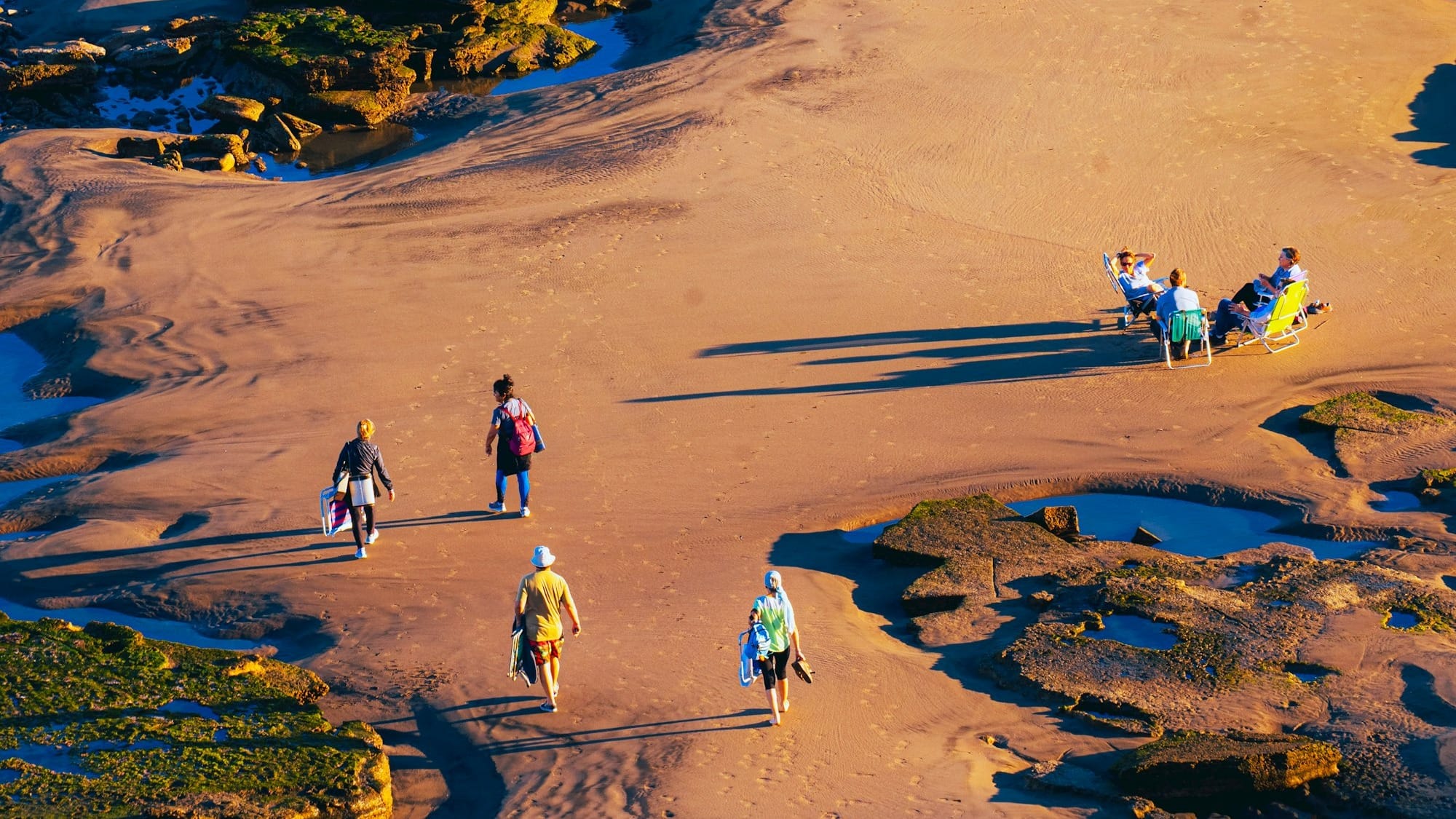 People walking on a sandy beach with rock pools.