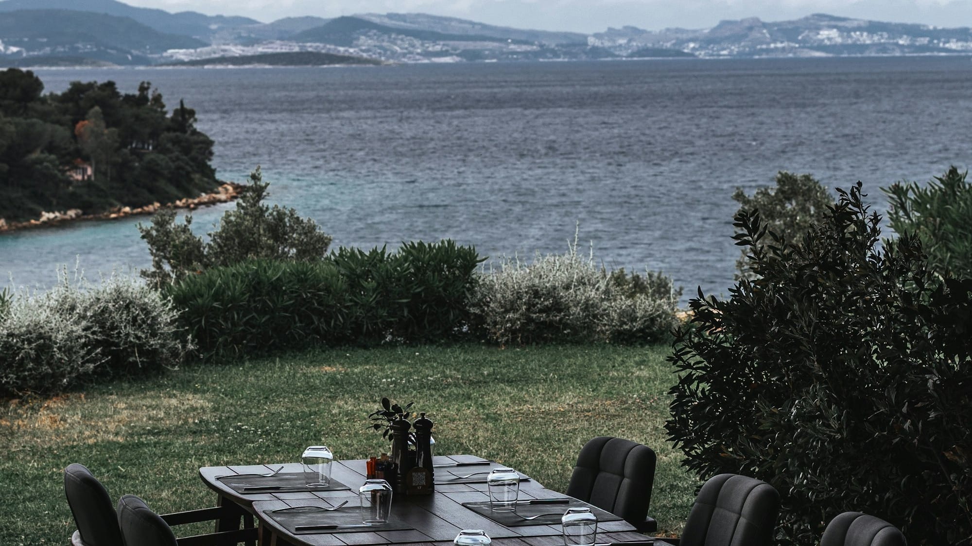 Outdoor dining table overlooking a serene sea and distant mountains.