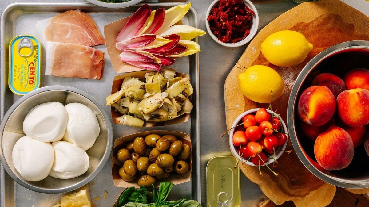 Platter of Mediterranean foods like Mozzarella, olives, endive, lemons and fruits on a table.