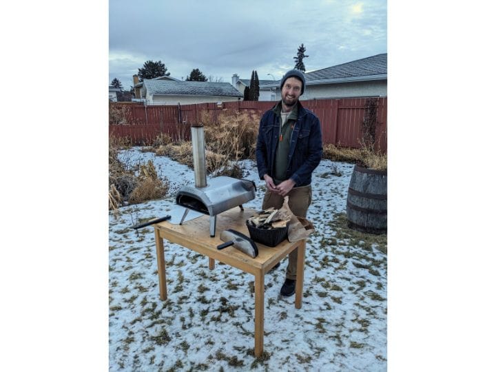 Man loads wood into a pizza oven outdoors in the snow.