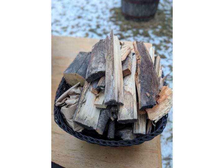 Black basket full of small pieces of wood on a table outside.