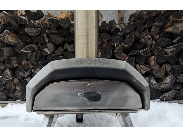 Steel Ooni Karu pizza oven in front of wood pile