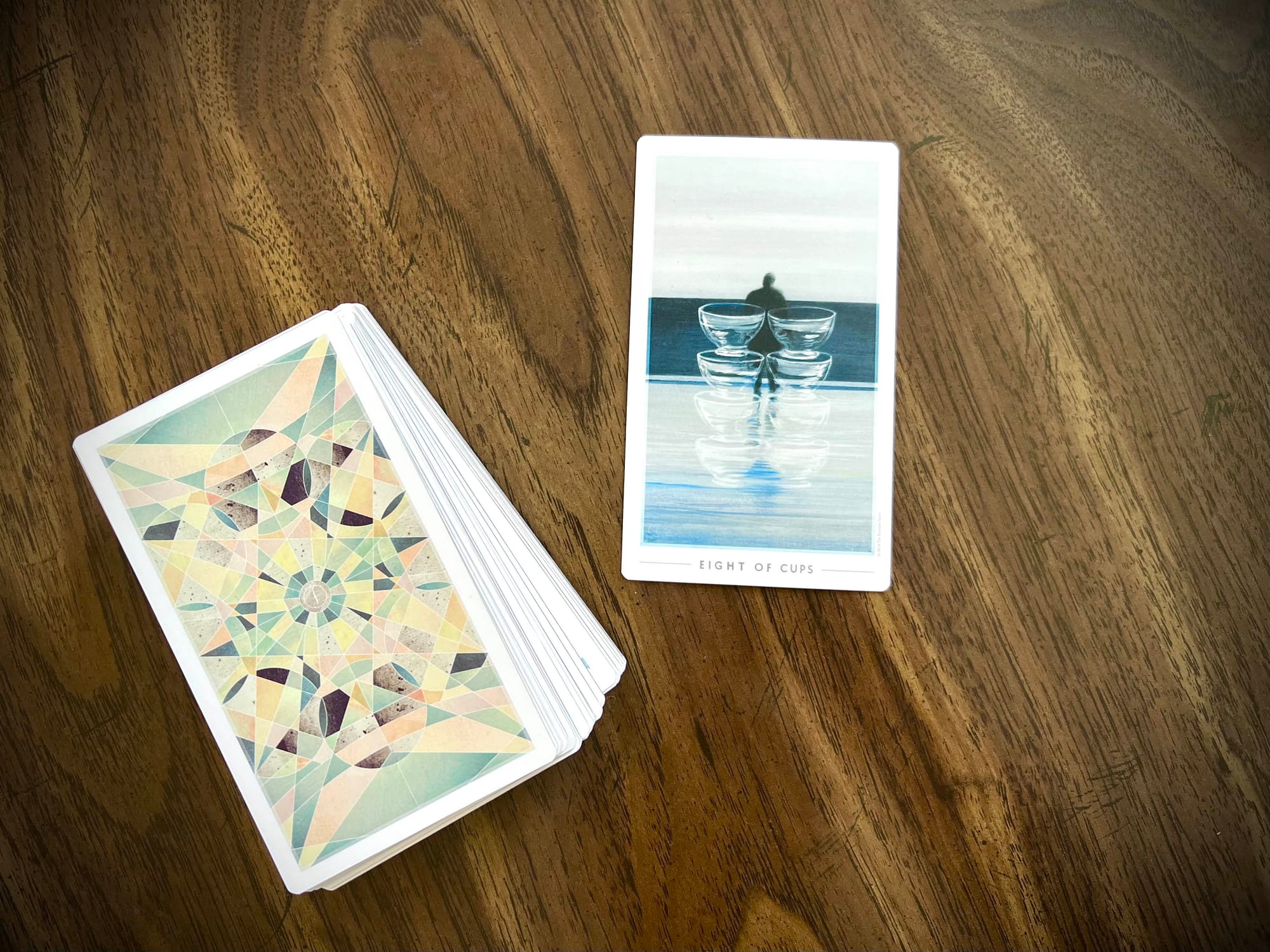On a wooden surface, the tarot card the Eight of Cups has been drawn from the Fountain deck