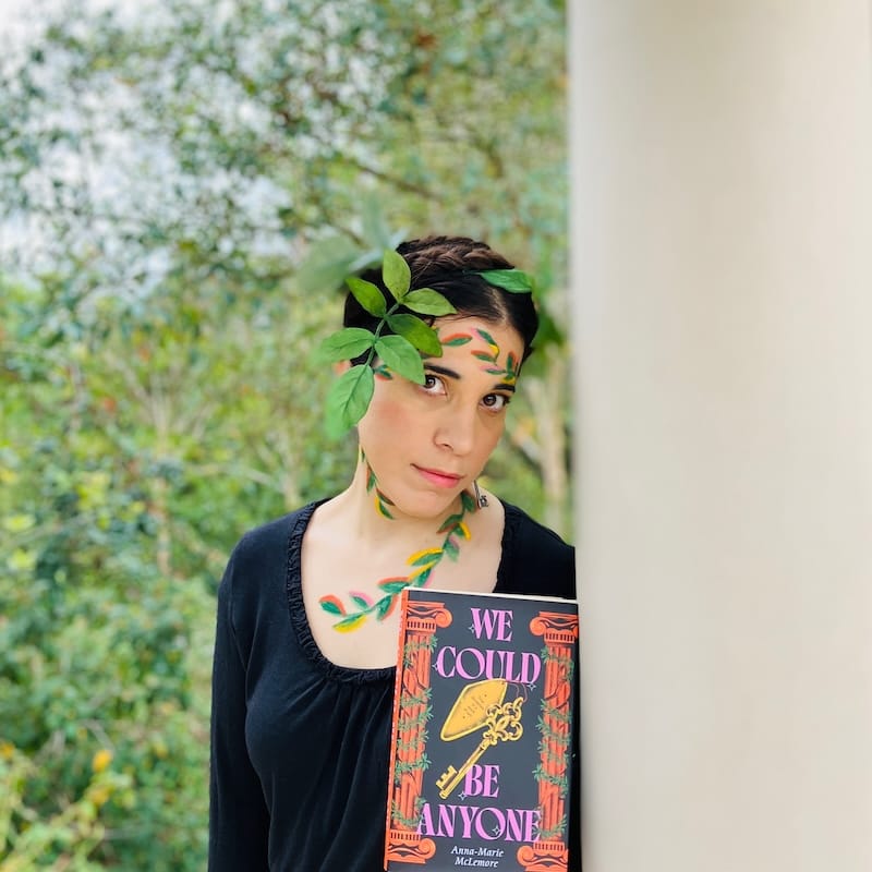 Author holding book with vining leaves painted on face and leaves woven into braided hair.