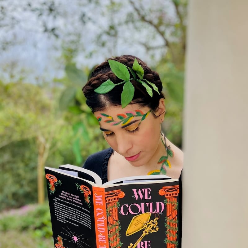 Author reading book with vining leaves painted on face and leaves woven into braided hair.