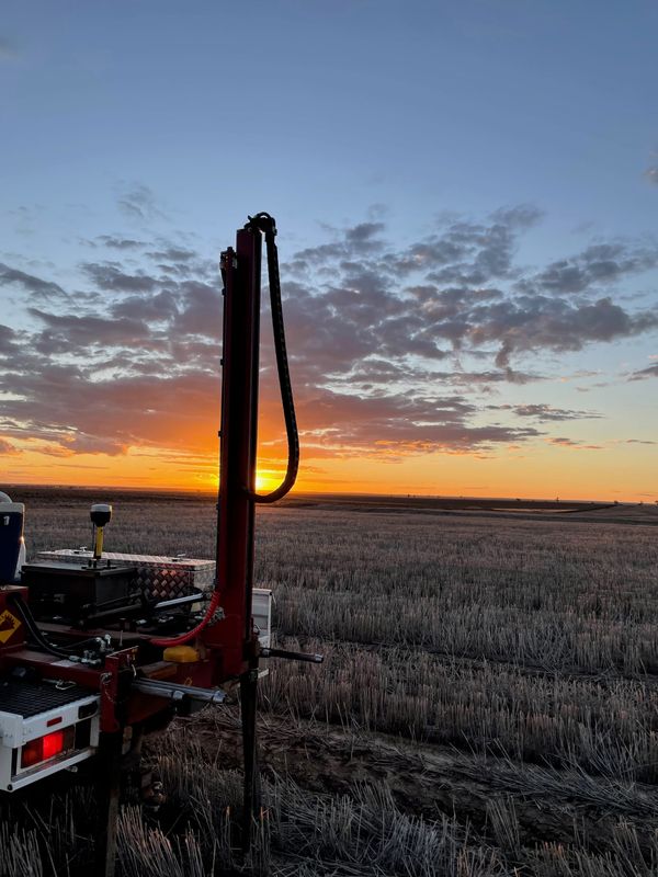 Picture of a soil sampling rig on the back of a ute taking a core from a field of harvested wheat at sunset.