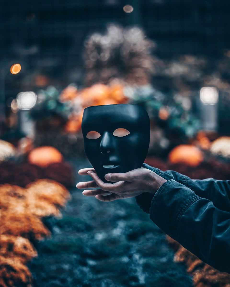 Hand holding a black mask in soft focus background, representing solitude and inner reflection.