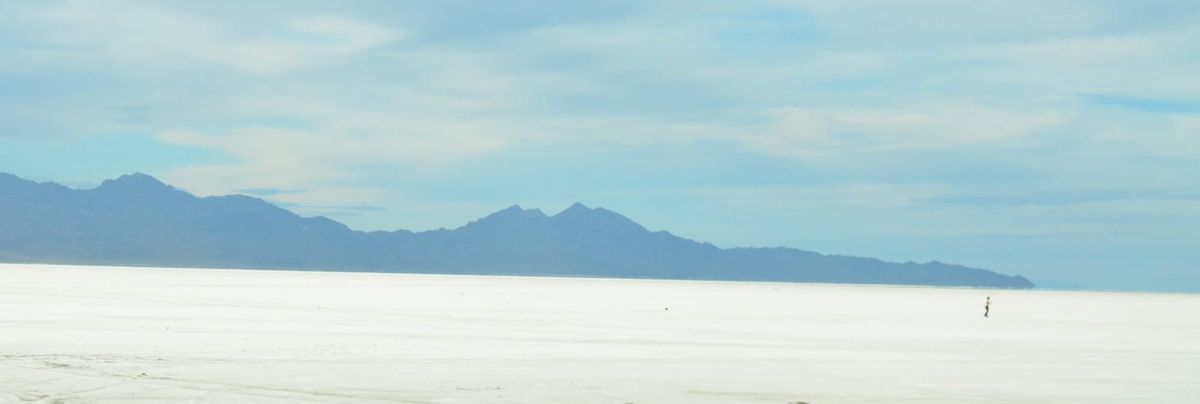 A figure walking through a wide expanse of white salt flats, with mountains in the distance