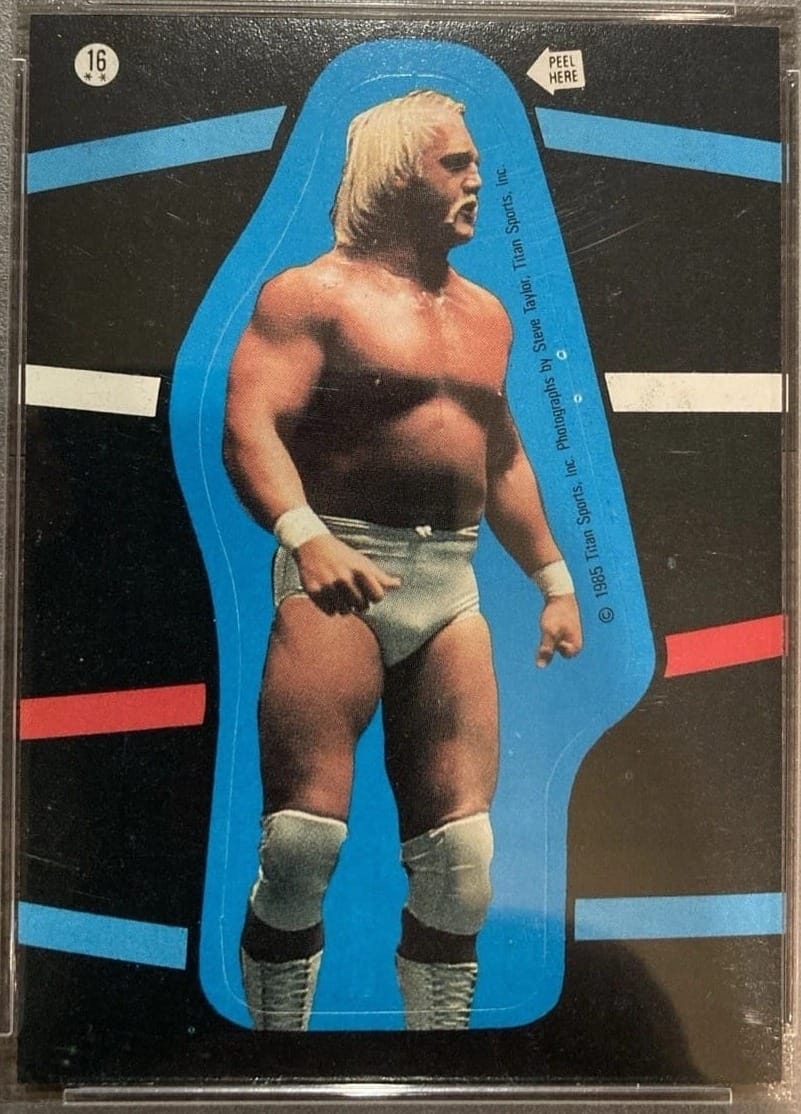 1985 O-Pee-Chee Hulk Hogan sticker No. 16, PSA 7: die-cut on black with the ring ropes behind him.