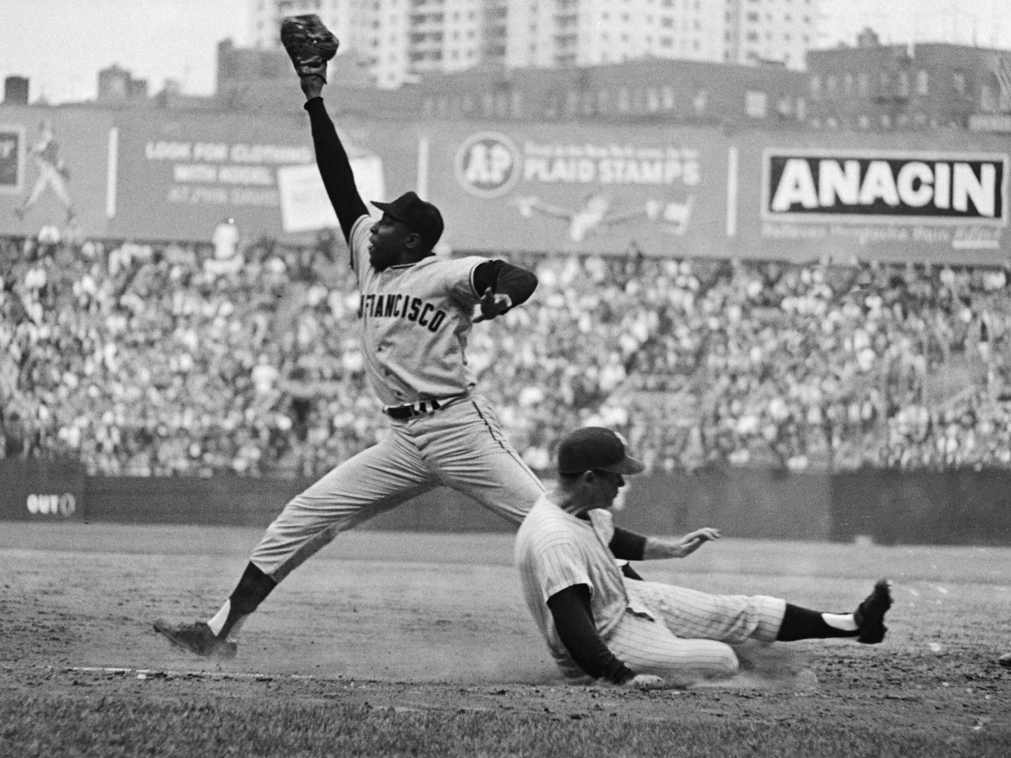 McCovey at first base in San Francisco road grays, stretching for a high throw with the runner sliding in — the glove on the right hand, the way a left-handed first baseman wears it.
