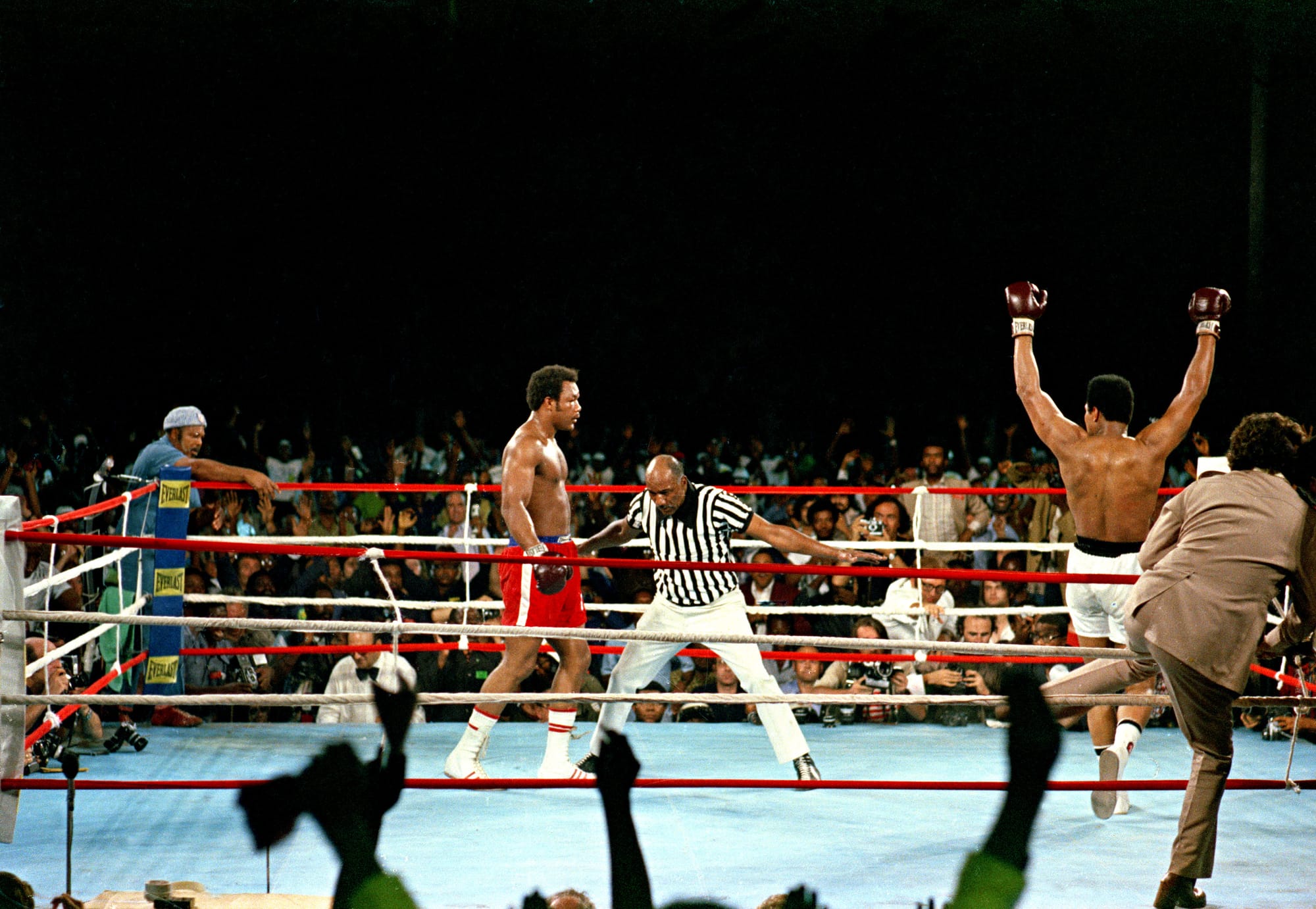 Ali raises his arms as Foreman stands in his corner.