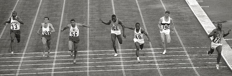 Bob Hayes (702), in lane 1 along the inside rail, breaks the tape in the 100-meter final, Oct. 15, 1964. (Photo: Mario De Biasi and Giorgio Lotti / Mondadori, public domain)