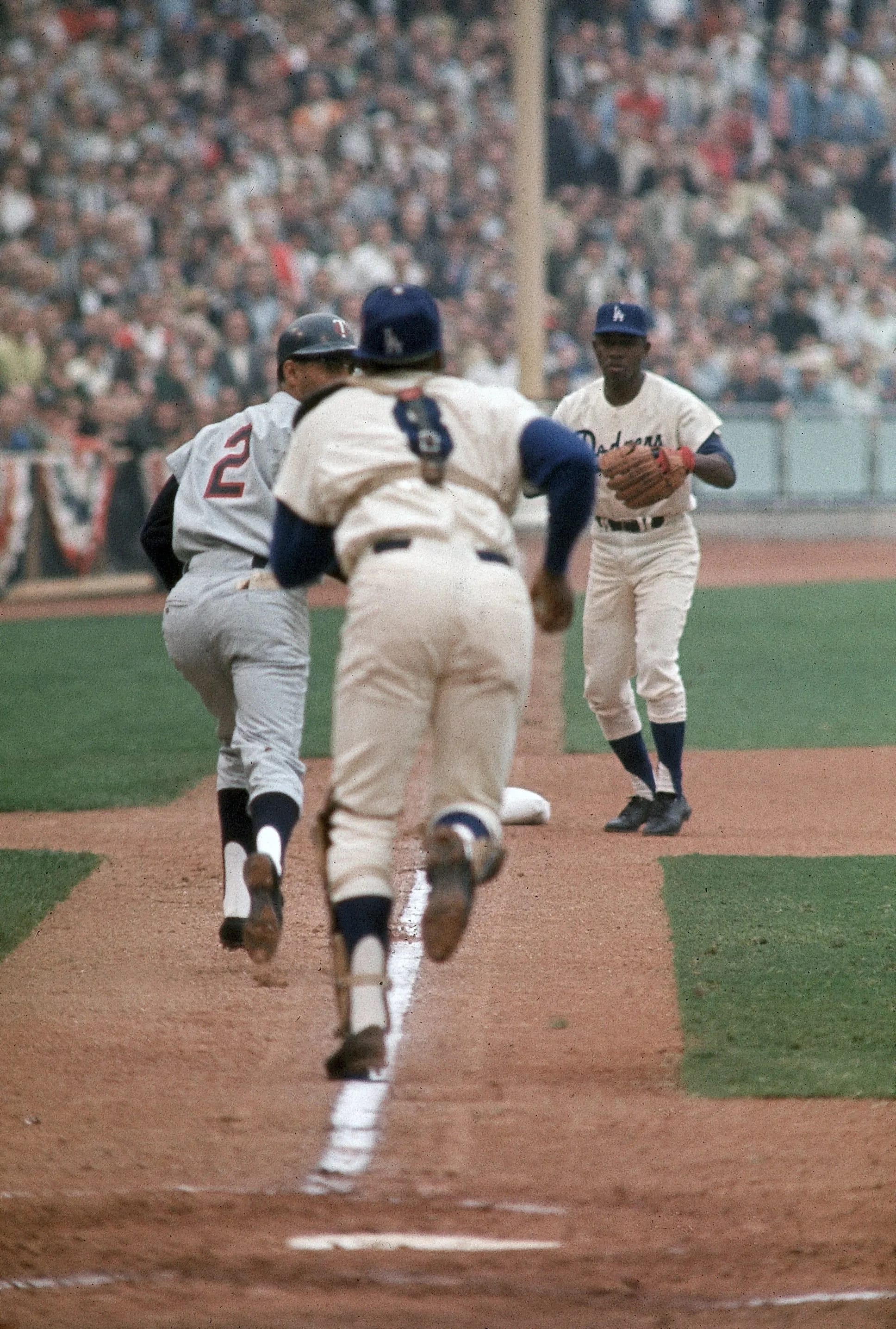 Zoilo Versalles (2) runs up the first-base line at Dodger Stadium, where the Dodgers won all 3 middle games. Catcher John Roseboro (8) trails the play.