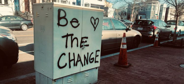 graffiti reading BE THE CHANGE with a heart sprayed on a metal electrical box on a city street