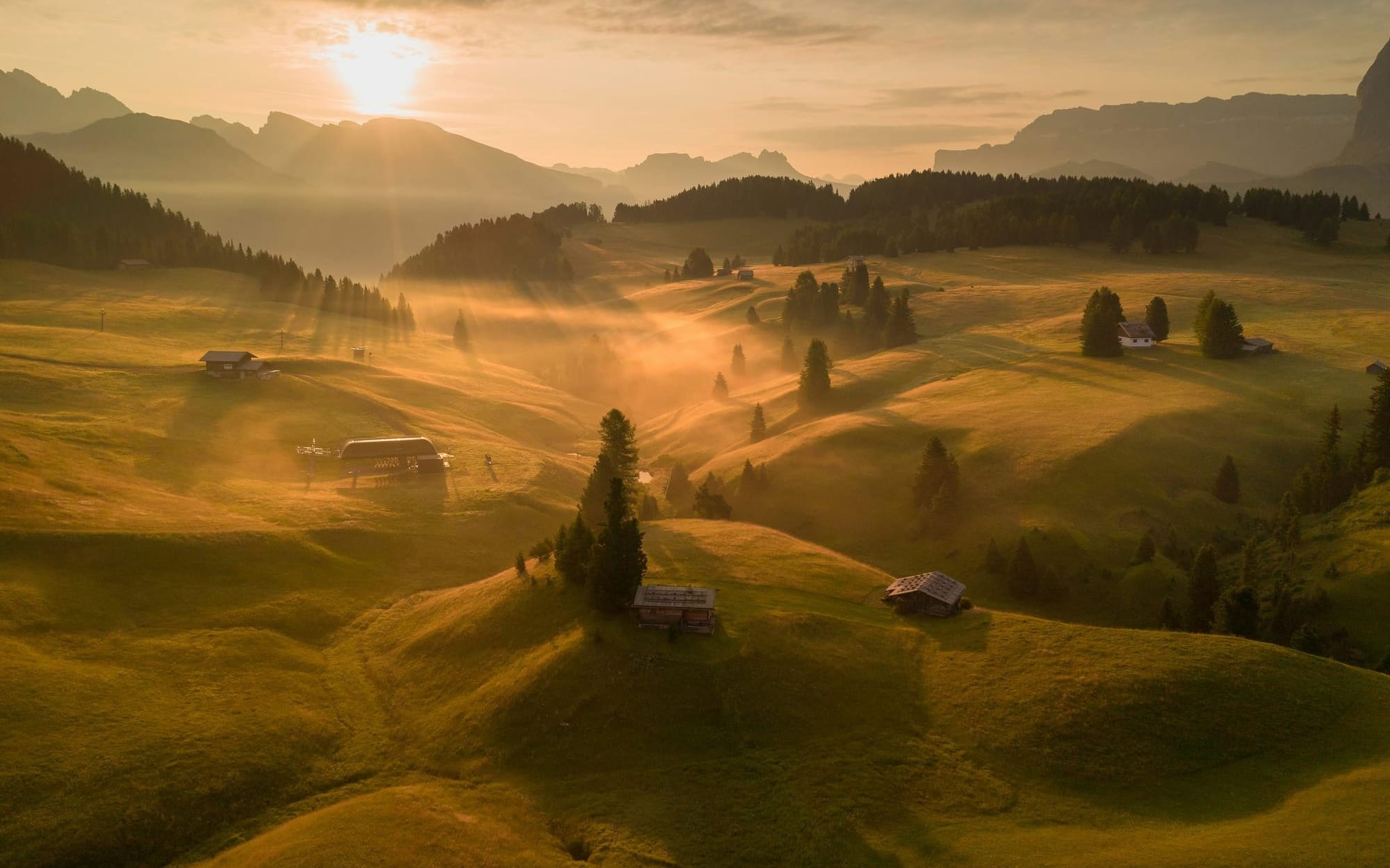 • A sweeping aerial view of misty alpine meadows and rolling green hills illuminated by warm golden sunrise light, symbolizing foundational wellness and circadian rhythm integration.