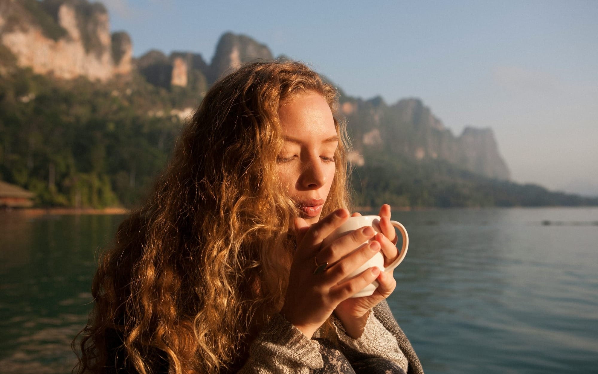 Woman enjoying morning sunlight by a lake, symbolising the natural cortisol awakening response and the body’s circadian rhythm.