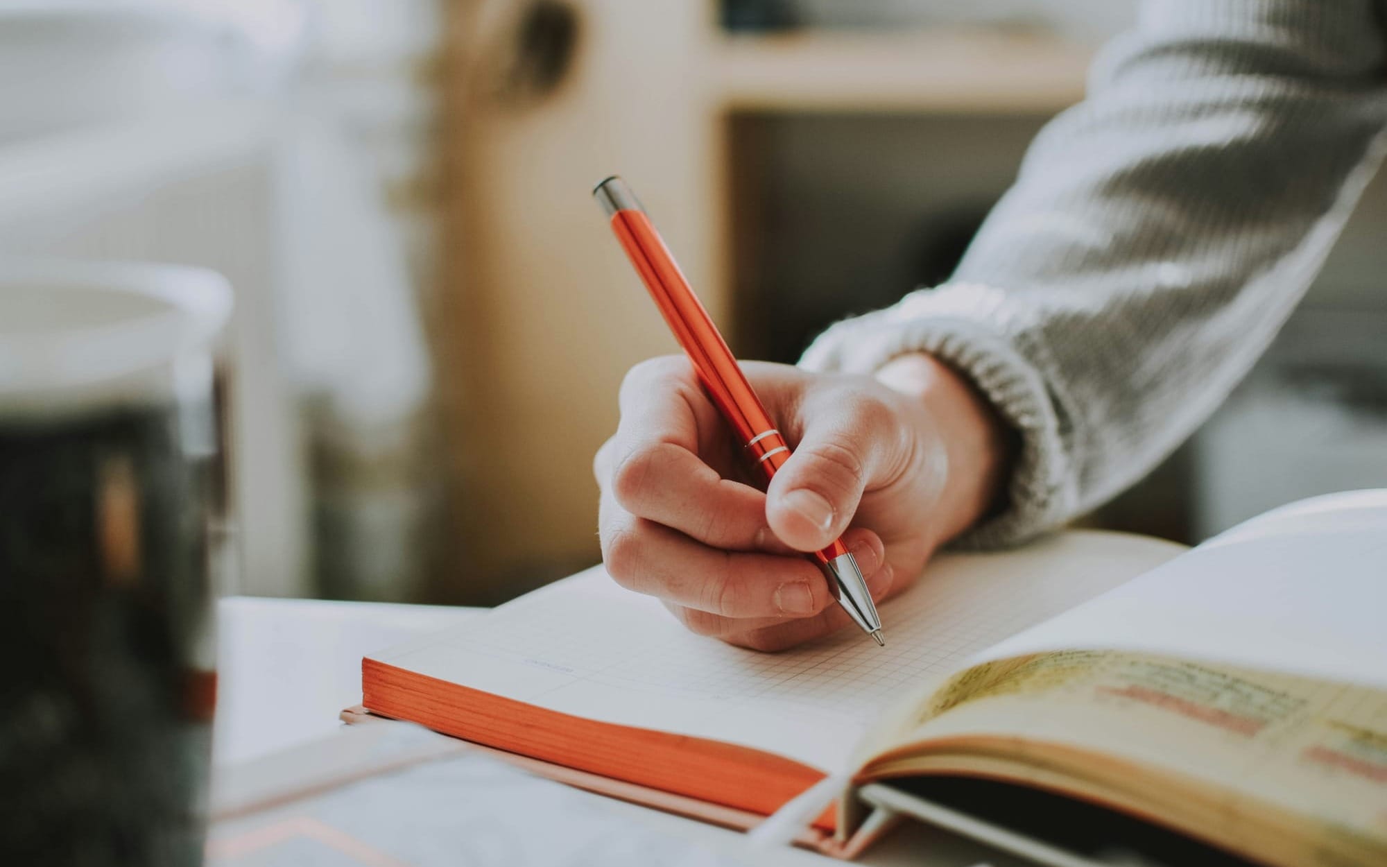 A calm close‑up of a hand writing in a notebook with a red pen — symbolizing clarity, purpose, and science‑rooted healing.