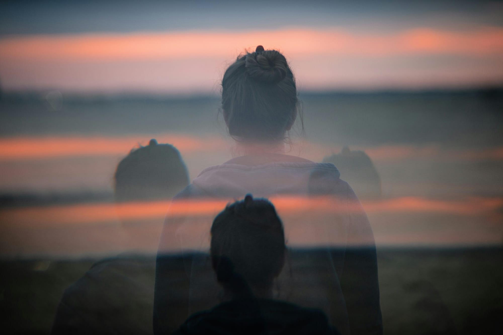 An abstract double exposure of a woman's silhouette layered over a sunset horizon, illustrating mental fatigue and a fractured psychological state.