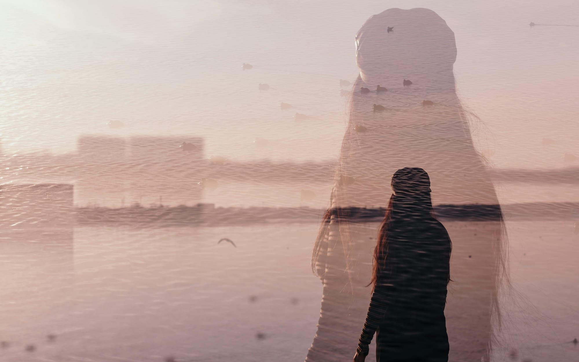 A double exposure photograph of a woman fading into a watery landscape, symbolizing depersonalization and the psychology of caregiver burnout.