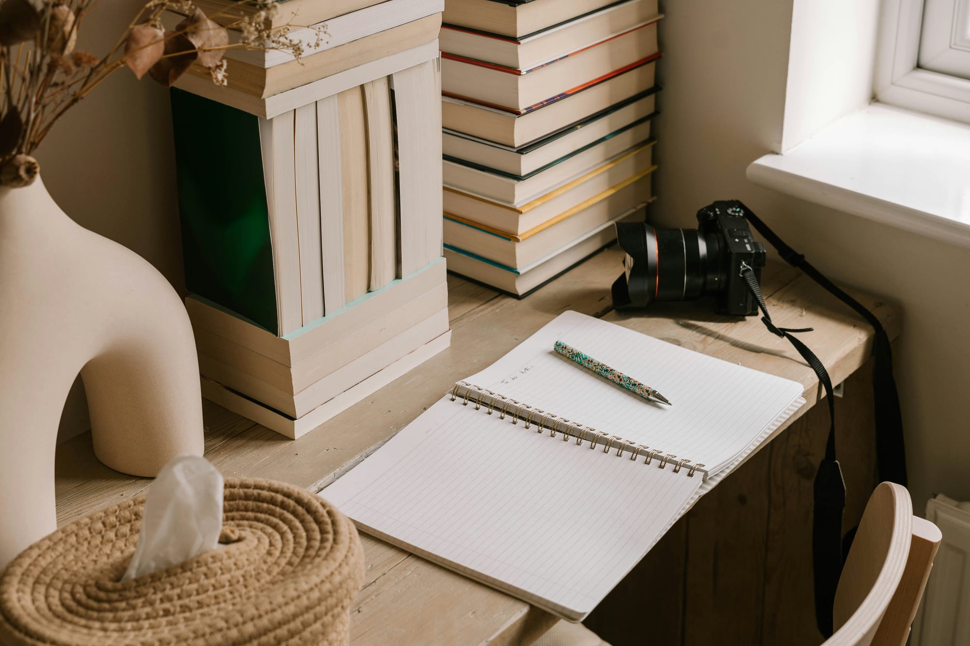 Calm wooden desk with open notebook, pen, and camera beside stacked books — a serene workspace symbolizing reflection, learning, and science‑rooted creativity.