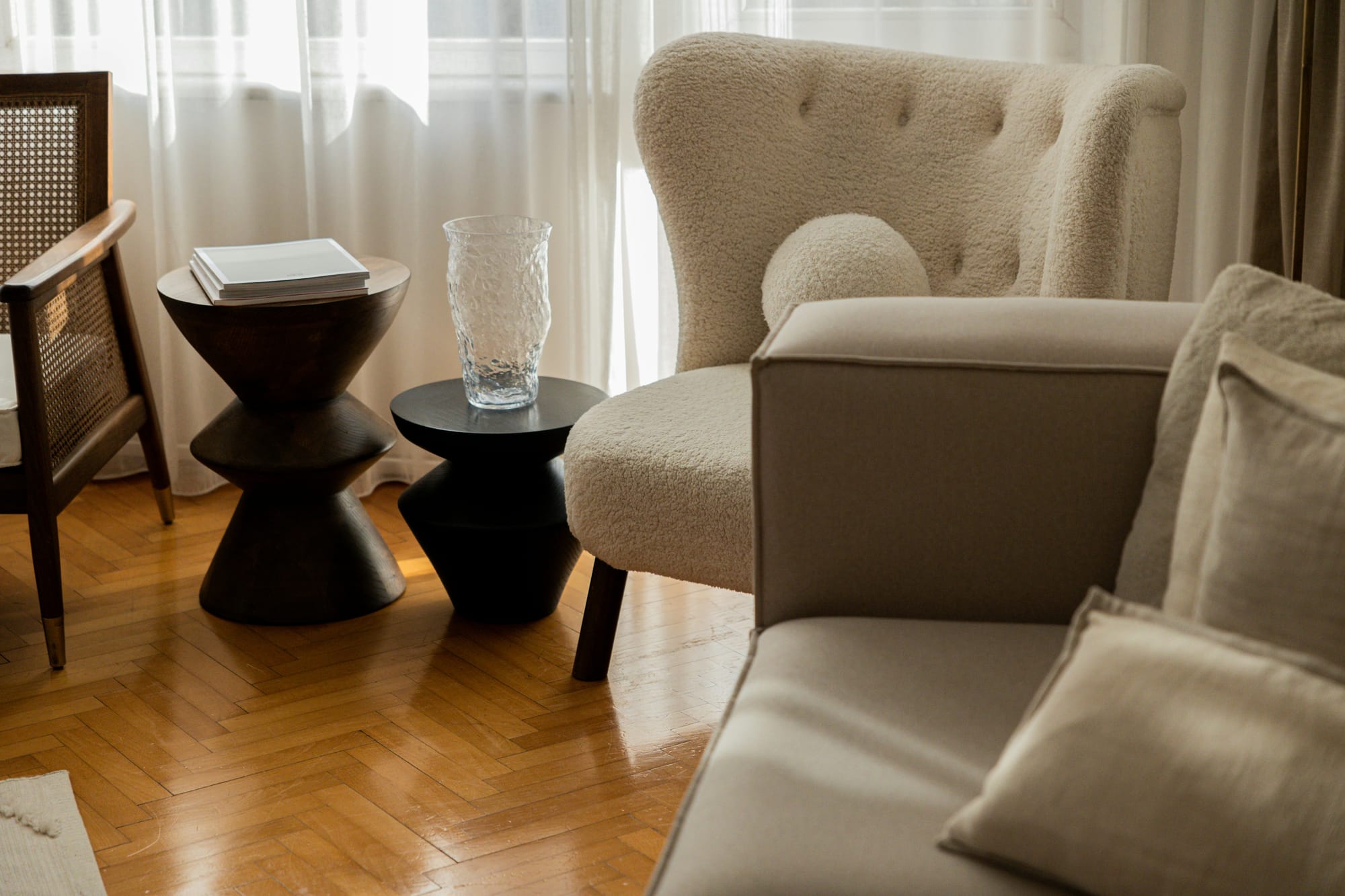 A cozy, premium interior nook featuring a soft white boucle armchair, natural wooden chevron floors, and minimalist side tables, evoking a comforting state of peaceful solitude.
