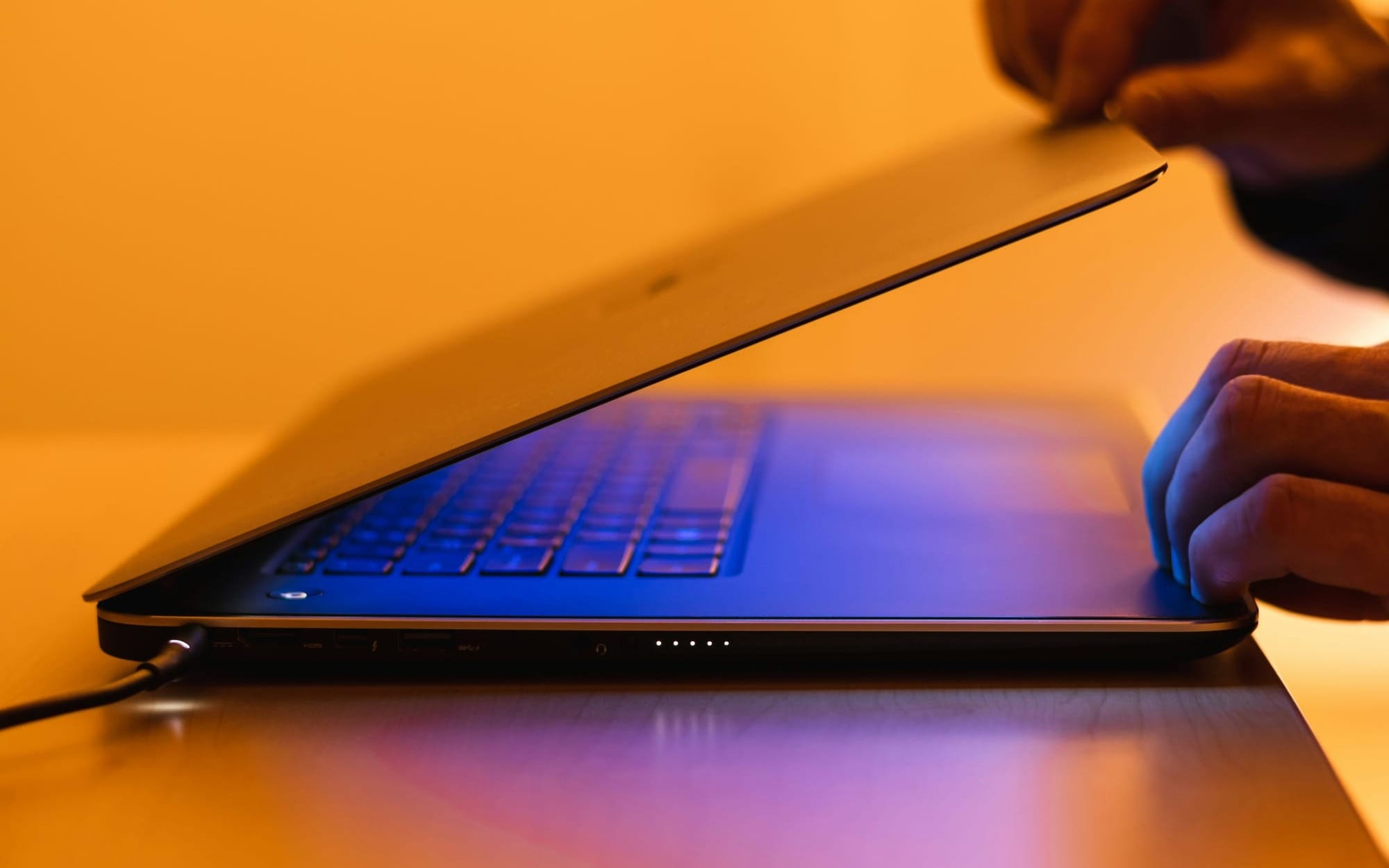 A close-up shot of a person's hands closing a laptop screen, with the blue light of the keyboard contrasting against warm ambient lighting, representing digital boundary setting.