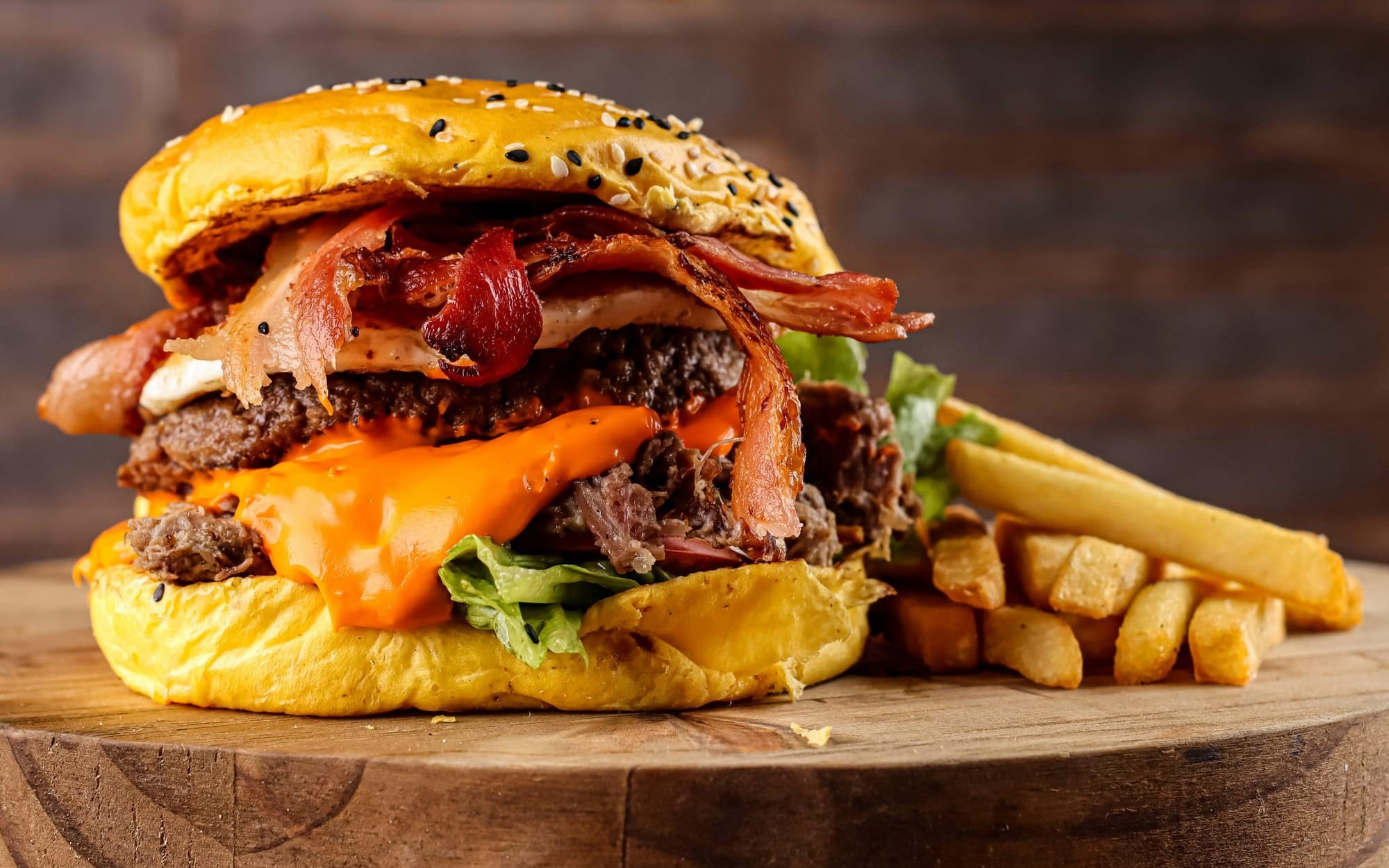 A close-up of a double cheeseburger with bacon and a side of french fries on a wooden board, illustrating ultra-processed foods that act as vagus nerve disruptors.