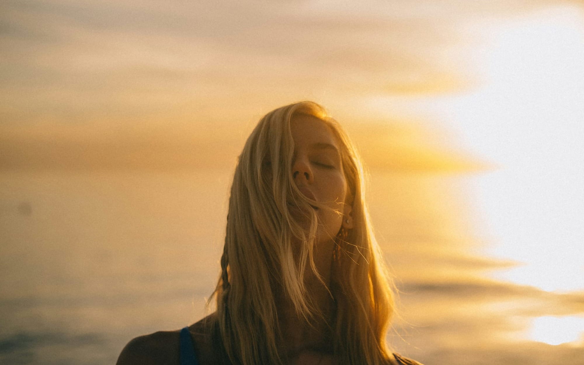 A peaceful close-up profile of a woman with closed eyes bathed in soft golden sunset light, evoking a sense of deep inner child healing and emotional introspection.
