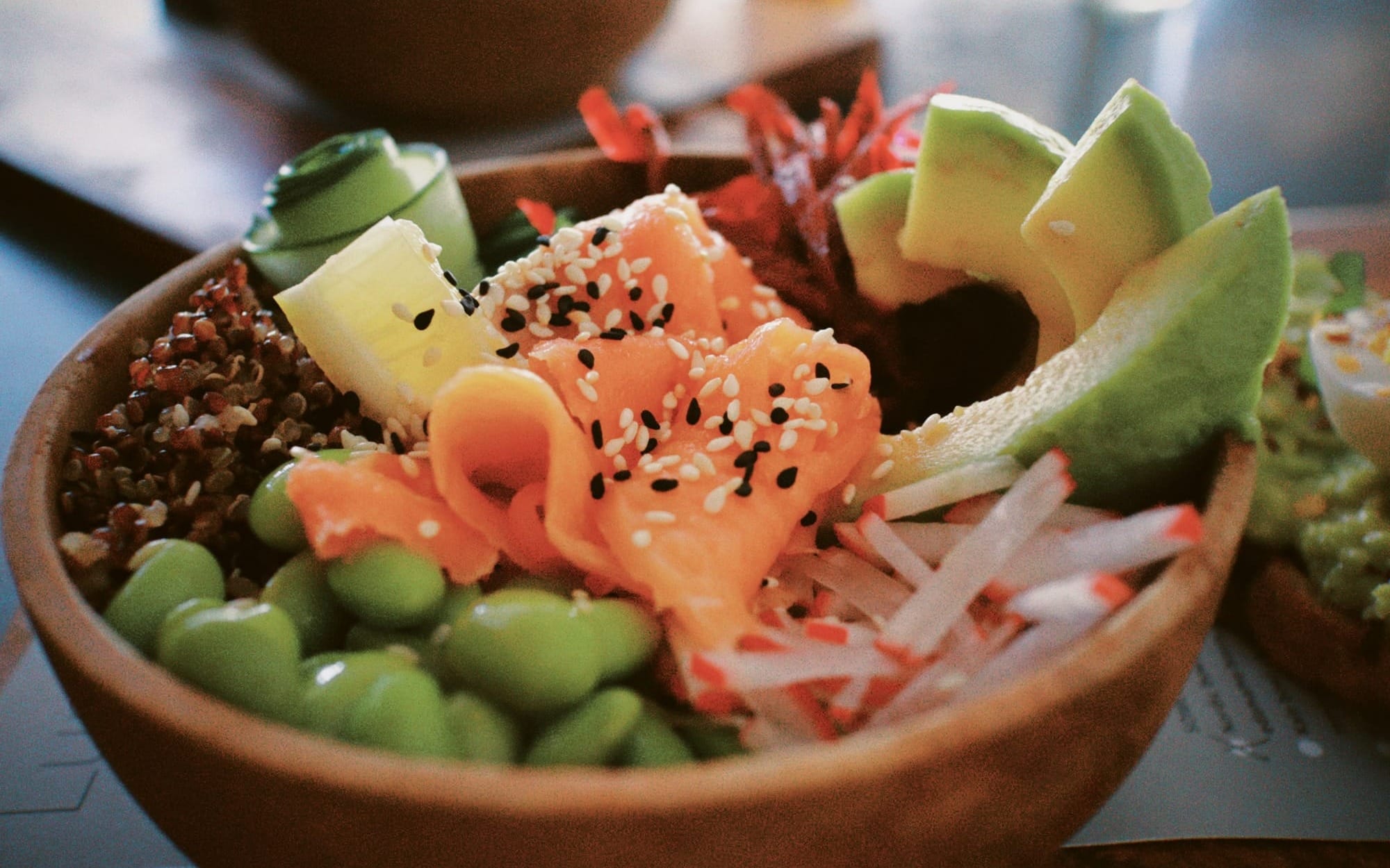 A close-up of a nutritious poke bowl filled with fresh raw salmon, sliced avocado, edamame, and quinoa, representing rich dietary sources of omega-3 fatty acids.