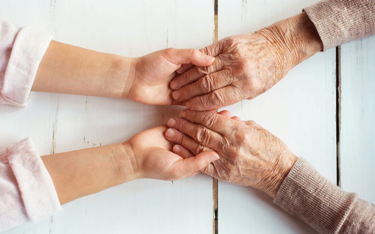 Young child's smooth hands cradling the wrinkled hands of an elderly grandmother on a white wooden table.