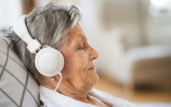1.  An elderly woman resting peacefully with her eyes closed while wearing white headphones, illustrating the calming effects of music therapy on the aging brain.