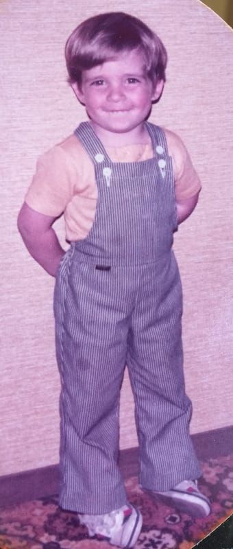 A very 70s-looking photo of a child wearing some dashing overalls and otherwise being adorable.
