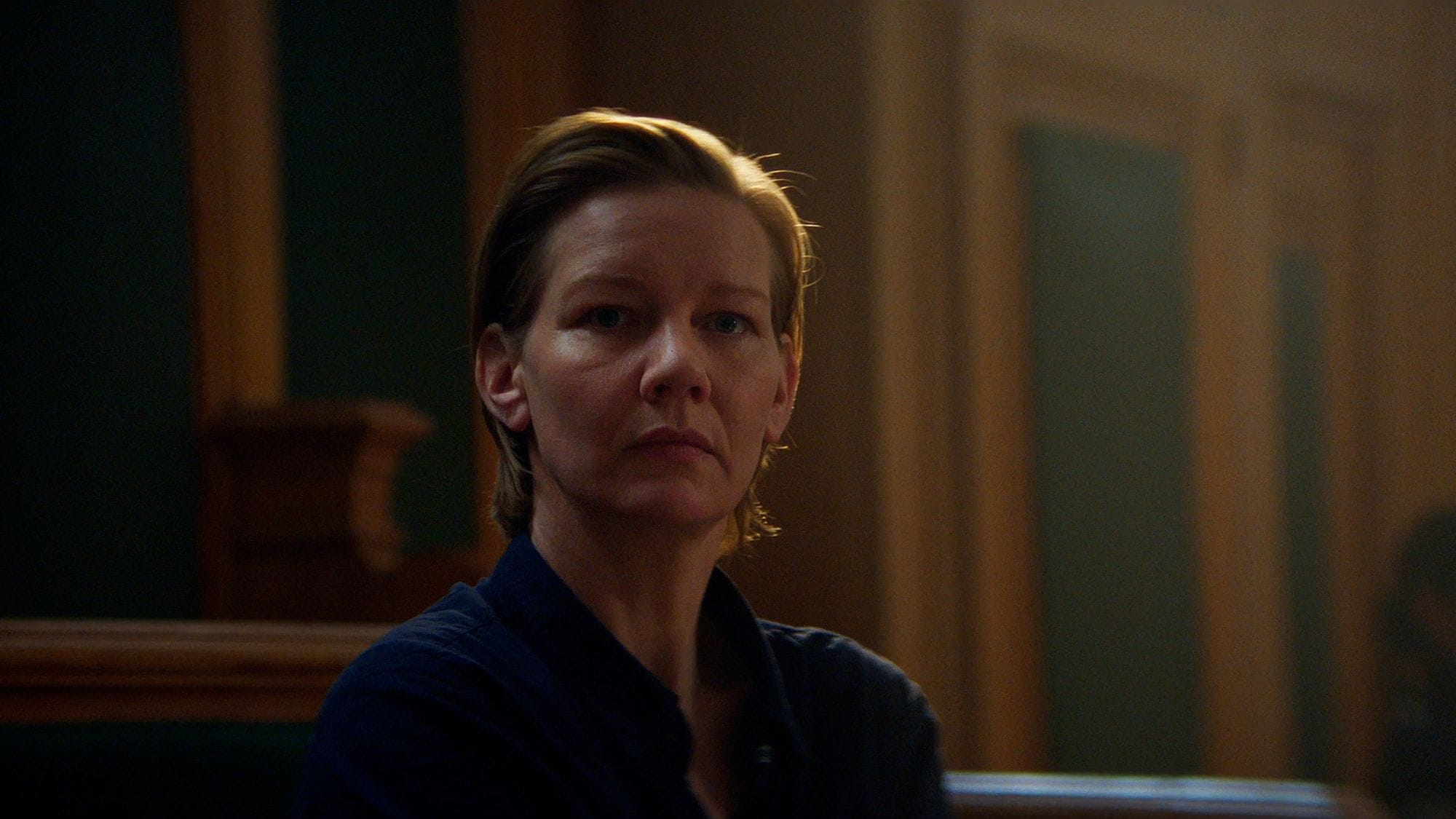 A white woman with short blonde hair sits in a courtroom. She is shot in close-up.