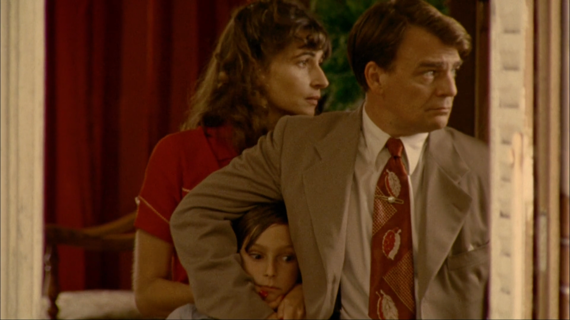 A man and a woman look off-camera to the right, while the man holds his son close to him.