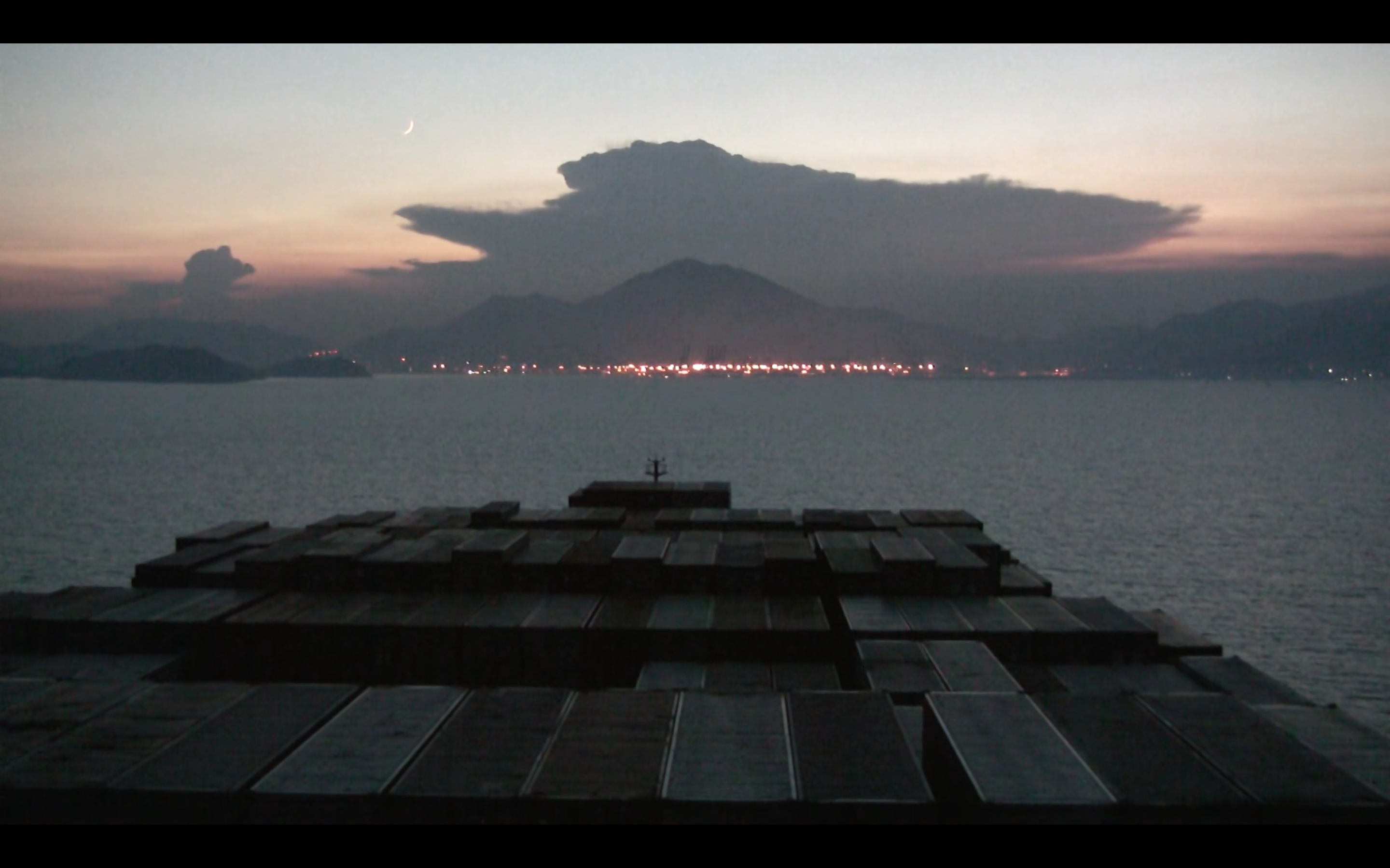 The ship approaches a city nestled at the foot of a mountain. It's twilight.