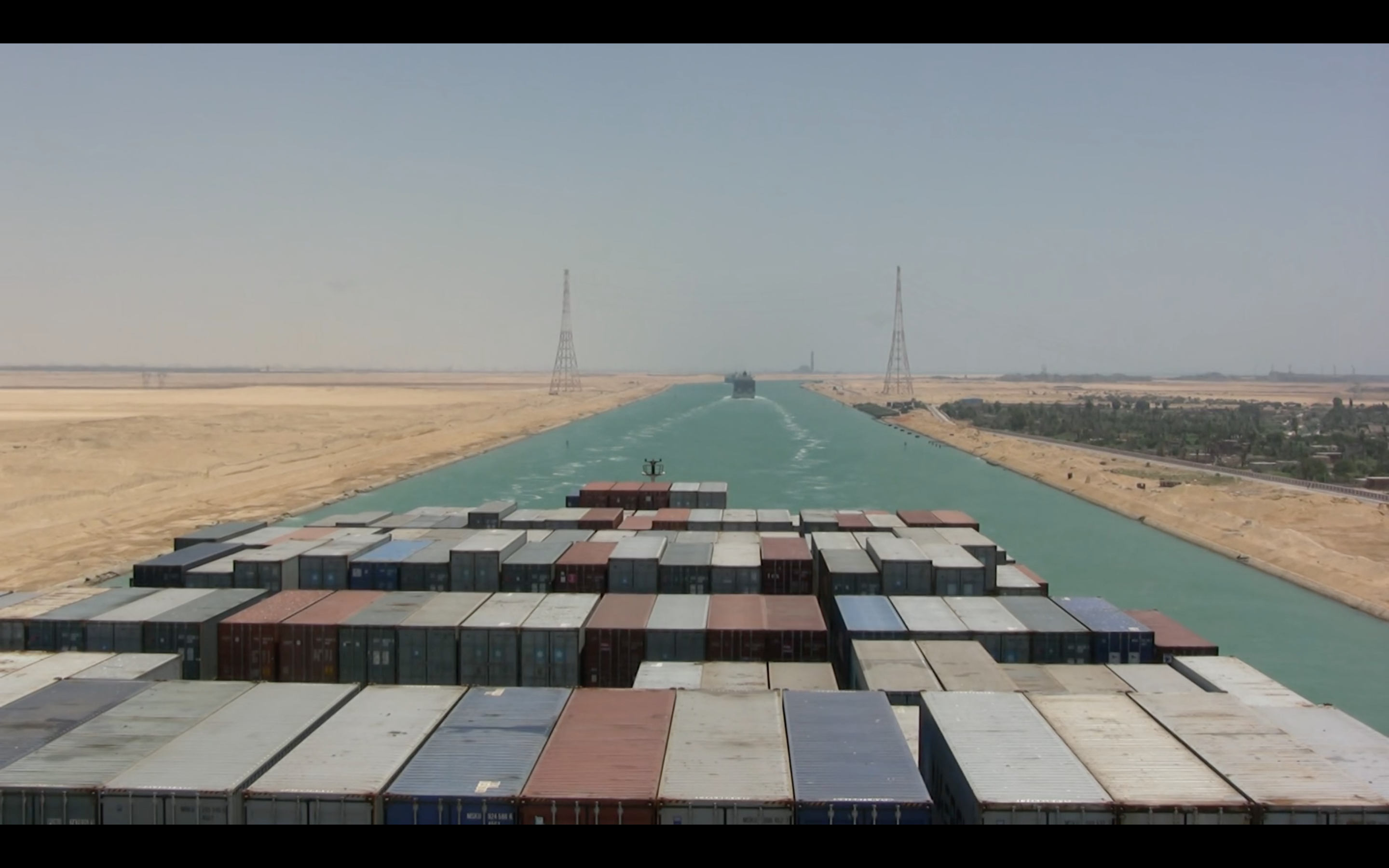 The ship makes its way through a narrow strip of blue water, desert on either side.