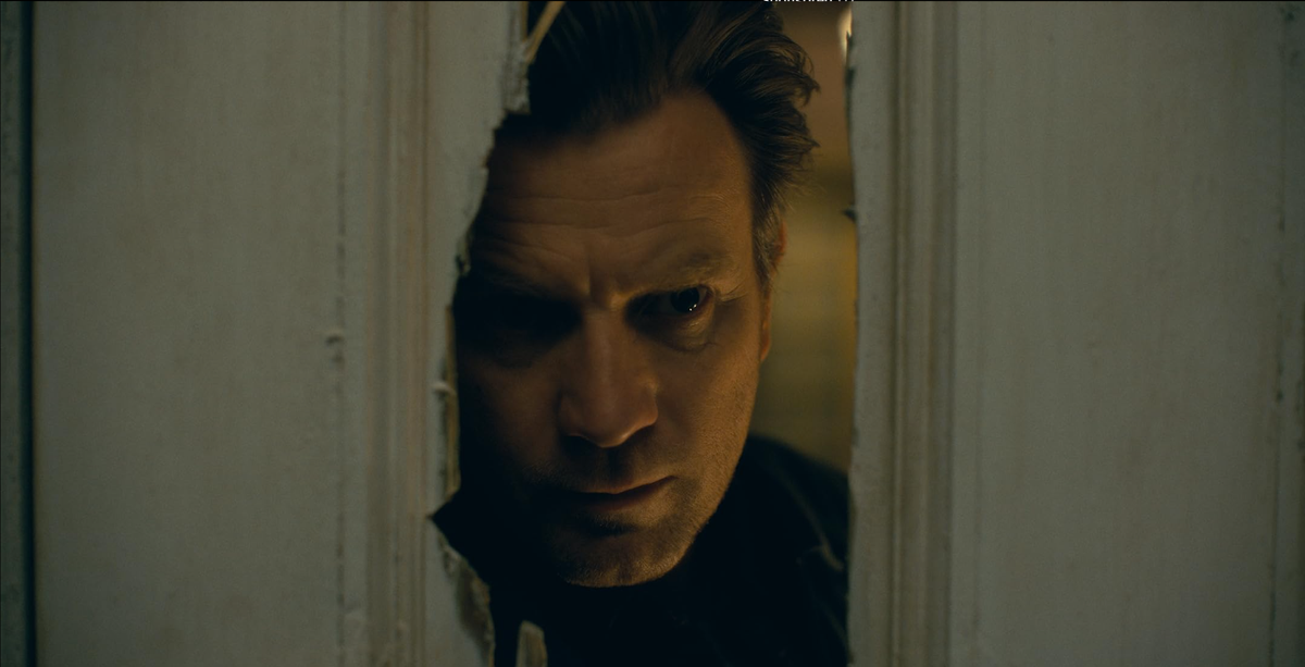 Dan (Ewan MacGregor) peers through a hole in a door put there by his axe-wielding father in The Shining.