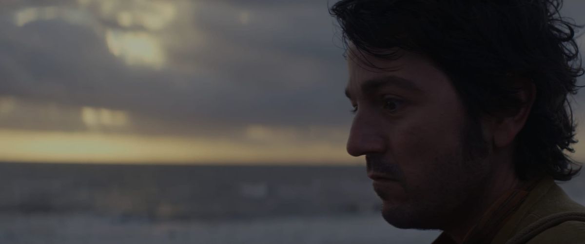 Cassian stares in a melancholy mood as the sun rises behind him. 
